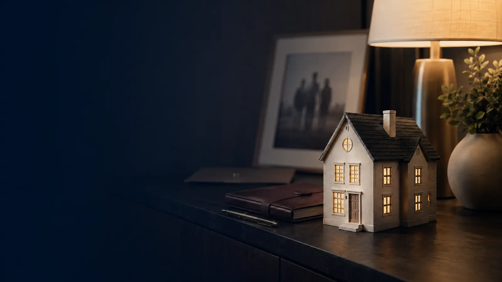 Life insurance to pay off a mortgage - Mallard Mortgage Protection Small lit model home on a dark console table representing life insurance to pay off a mortgage
